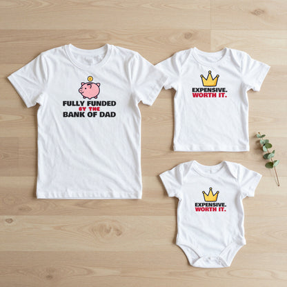 Bank of Dad & Expensive Worth It matching set flat lay on oak floor: grown-up tee, kids tee and baby grow
