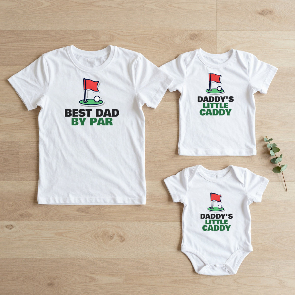 Best Dad By Par & Daddy's Little Caddy Golf matching set flat lay on oak floor: grown-up tee, kids tee and baby grow