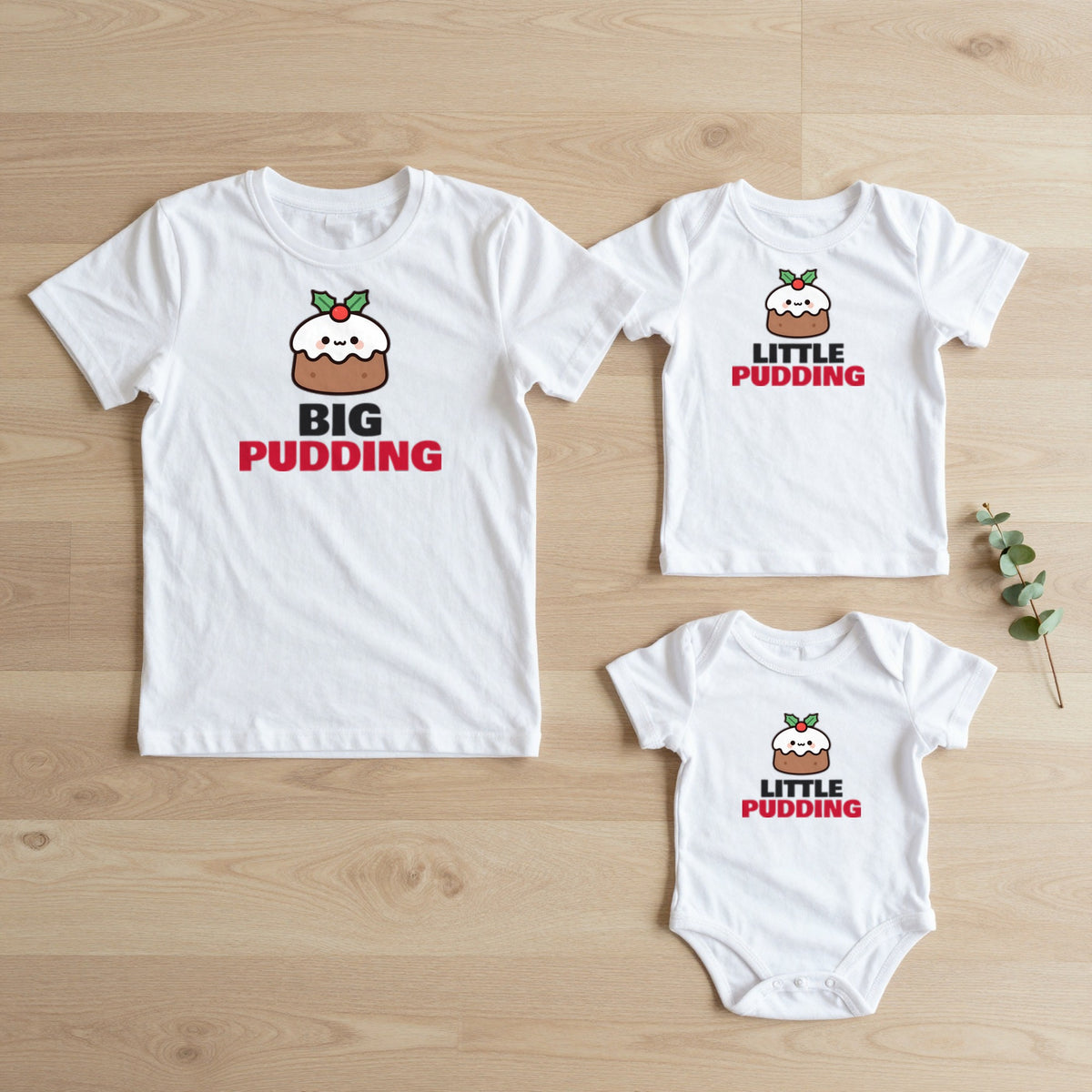 Big Pudding & Little Pudding Christmas matching set flat lay on oak floor: grown-up tee, kids tee and baby grow