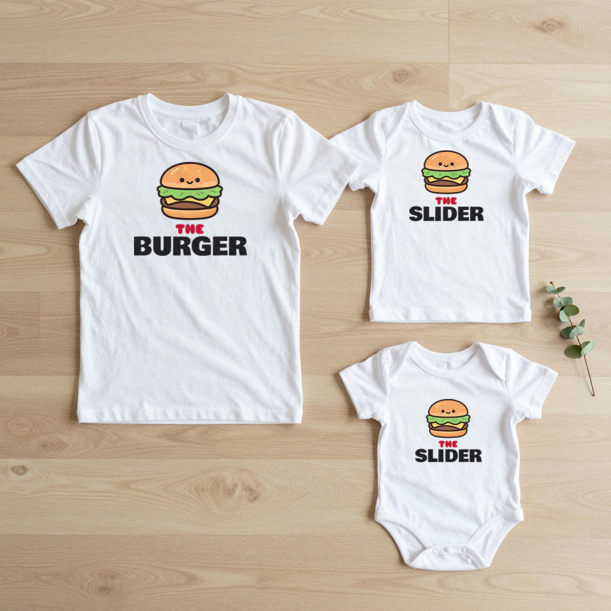 Burger & Slider matching set flat lay on oak floor: grown-up tee, kids tee and baby grow
