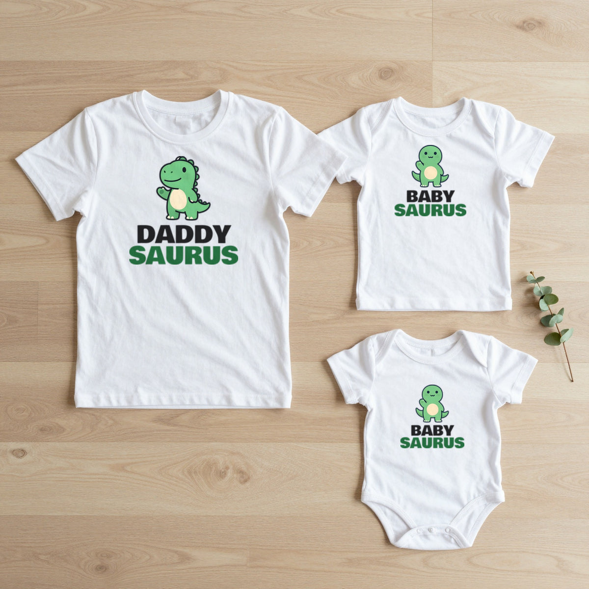 Daddysaurus & Babysaurus matching set flat lay on oak floor: grown-up tee, kids tee and baby grow