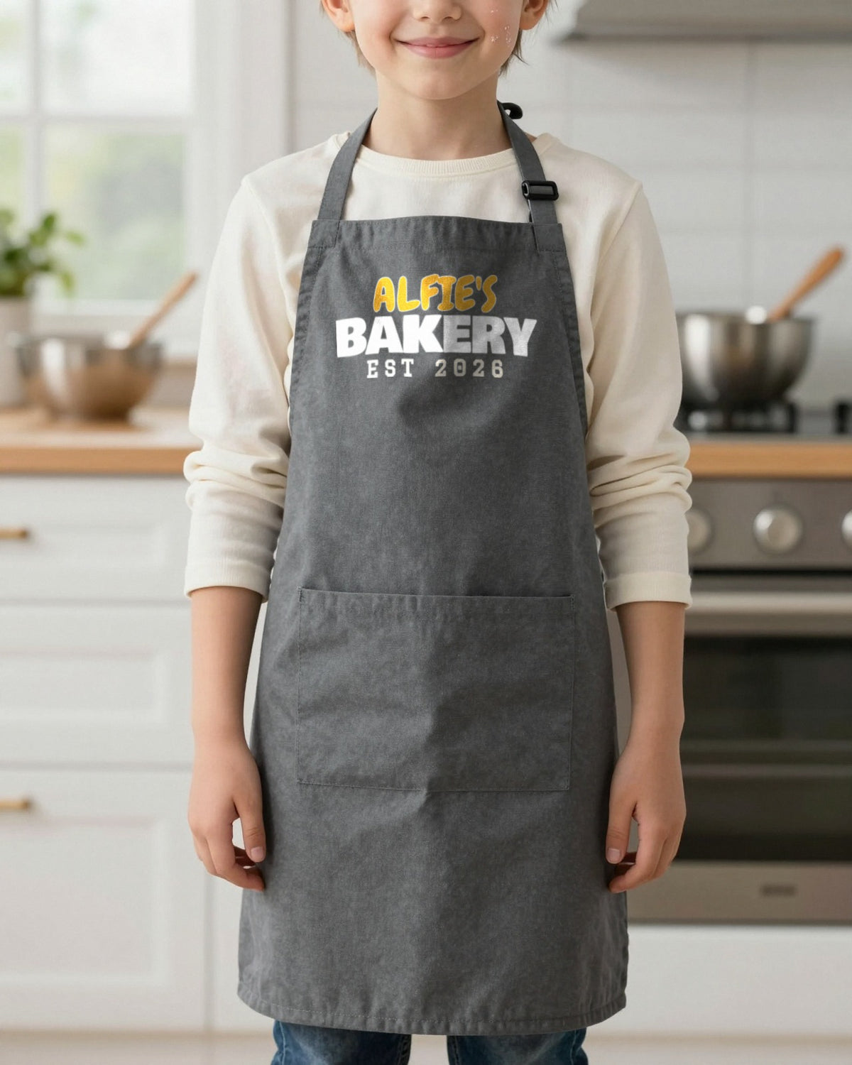 Kids Name's Bakery Est Year kids apron in Dark Grey, worn, our photo