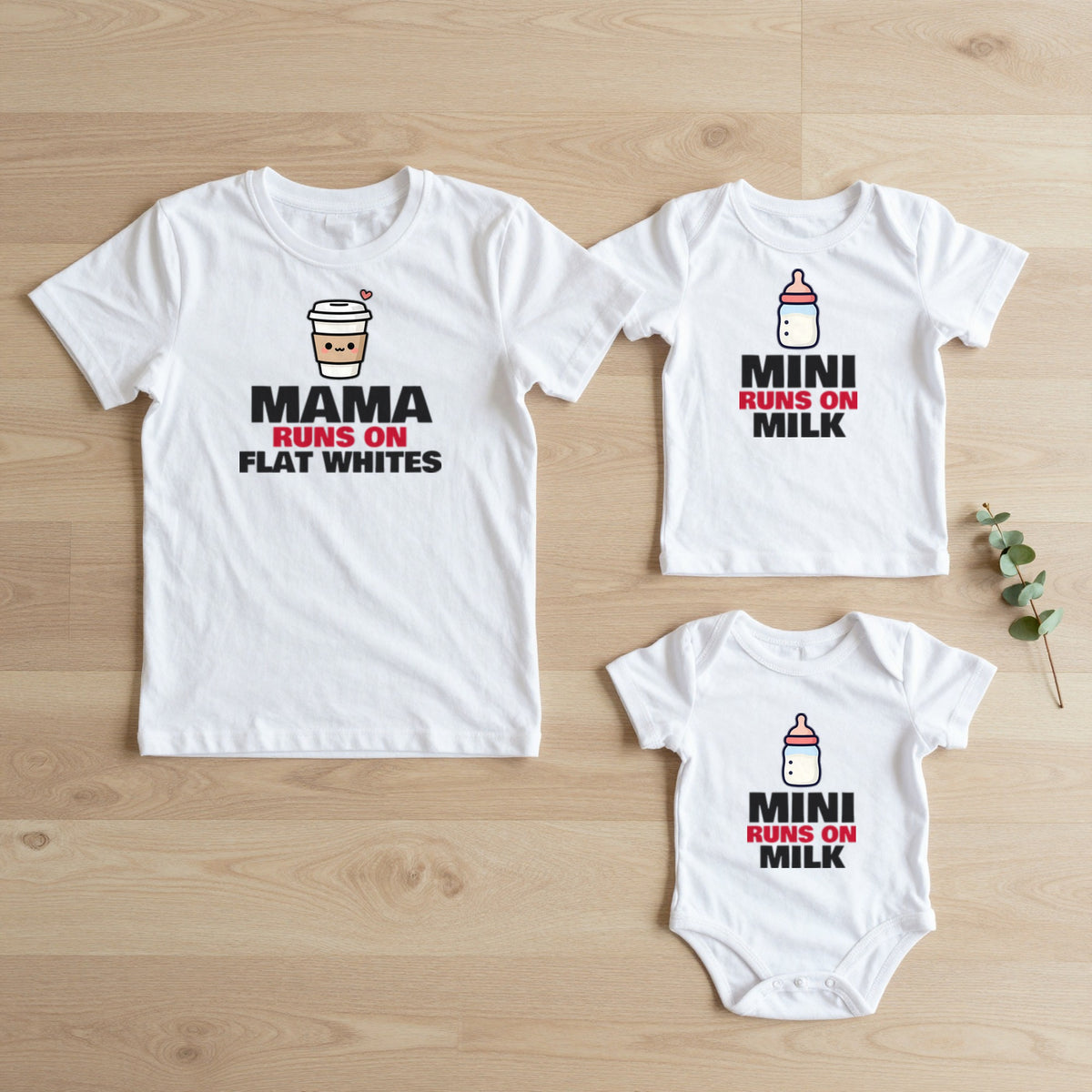 Mama & Mini | Runs on Flat Whites, Runs on Milk matching set flat lay on oak floor: grown-up tee, kids tee and baby grow