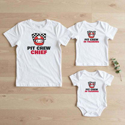 Pit Crew Chief & Pit Crew In Training matching set flat lay on oak floor: grown-up tee, kids tee and baby grow