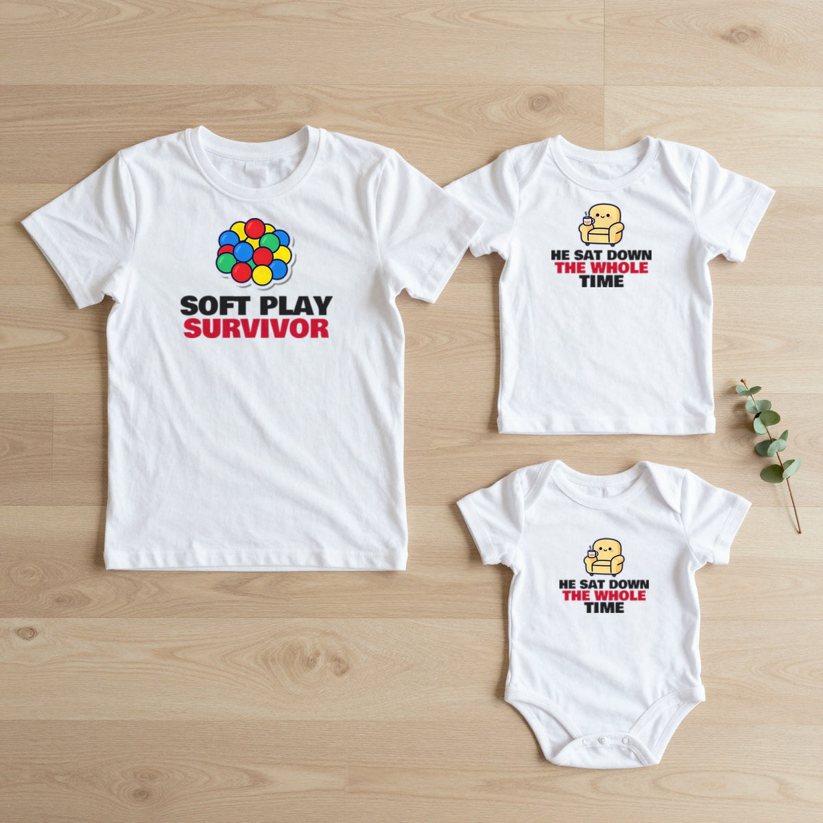 Soft Play Survivor & He Sat Down The Whole Time matching set flat lay on oak floor: grown-up tee, kids tee and baby grow