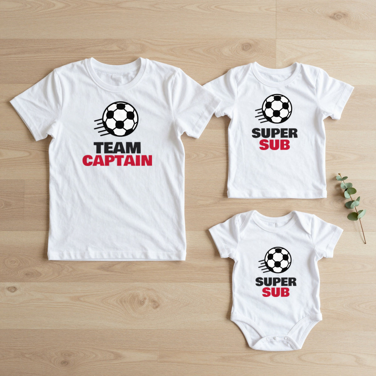 Team Captain & Super Sub Football matching set flat lay on oak floor: grown-up tee, kids tee and baby grow