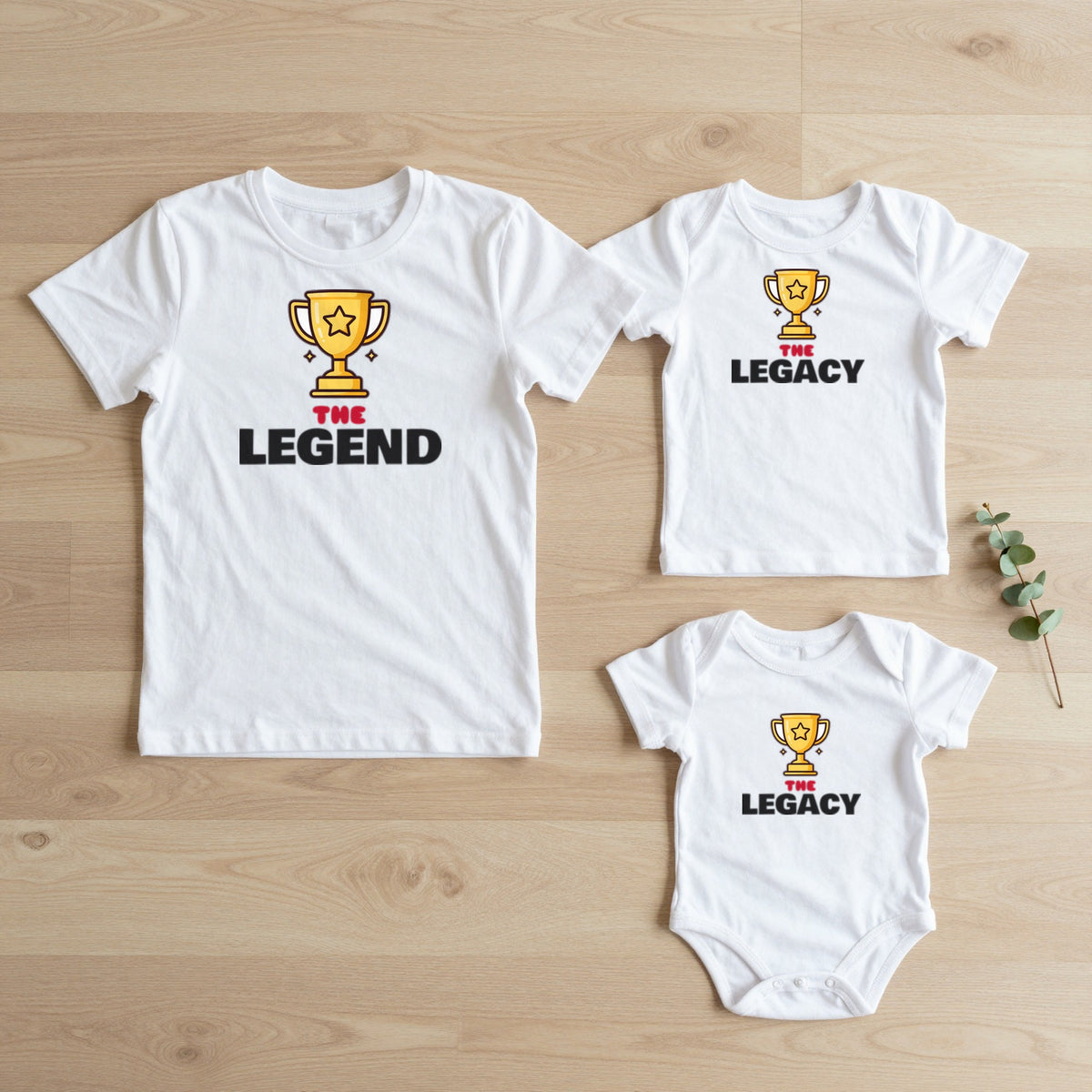 The Legend & The Legacy matching set flat lay on oak floor: grown-up tee, kids tee and baby grow
